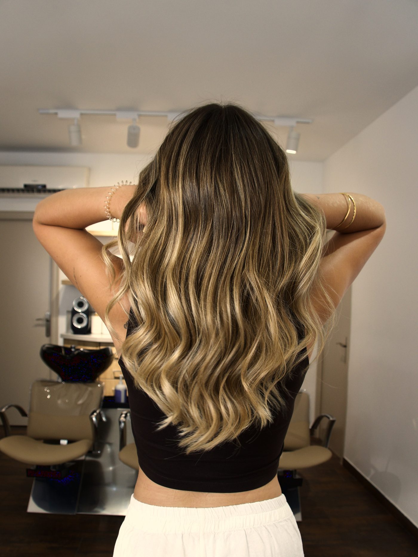 Balayage rubio sobre melena larga con ondas, vista de espaldas en el salón